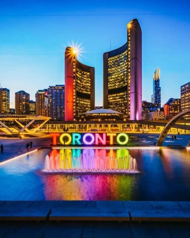 Toronto sign with colorful lights reflected in water at dusk, surrounded by illuminated downtown skyscrapers