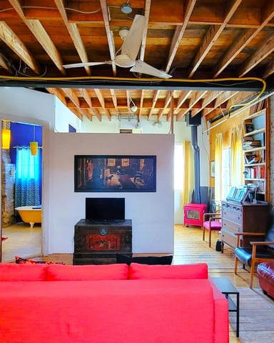 Open loft living room with red sofa, exposed wooden beams, artwork, and colorful modern furnishings
