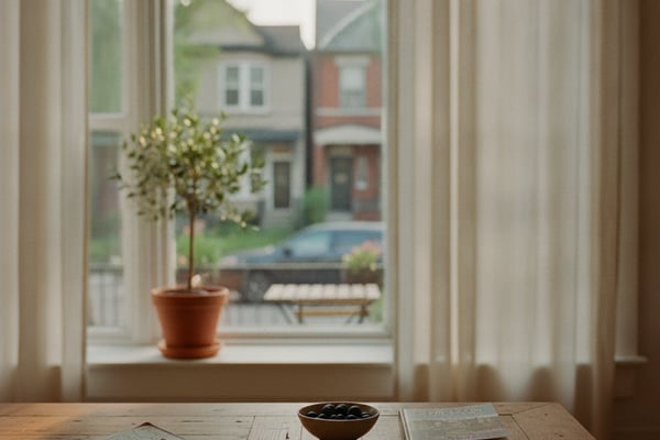 Wooden desk with books and papers near arched window with sheer curtains overlooking residential street