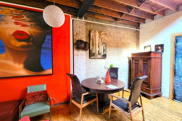 Industrial loft with red accent wall, round dining table, exposed brick, wooden beams, and contemporary art.