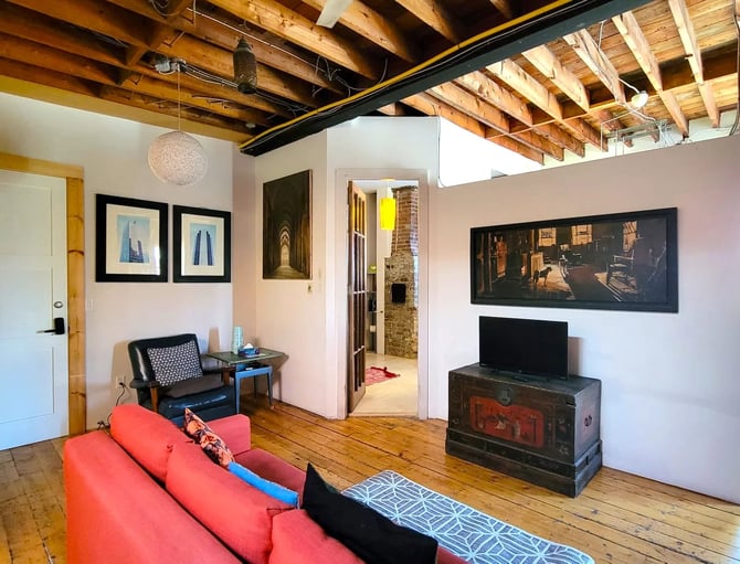 Loft living room with exposed wooden beams, red sofa, black armchair, and vintage trunk TV stand